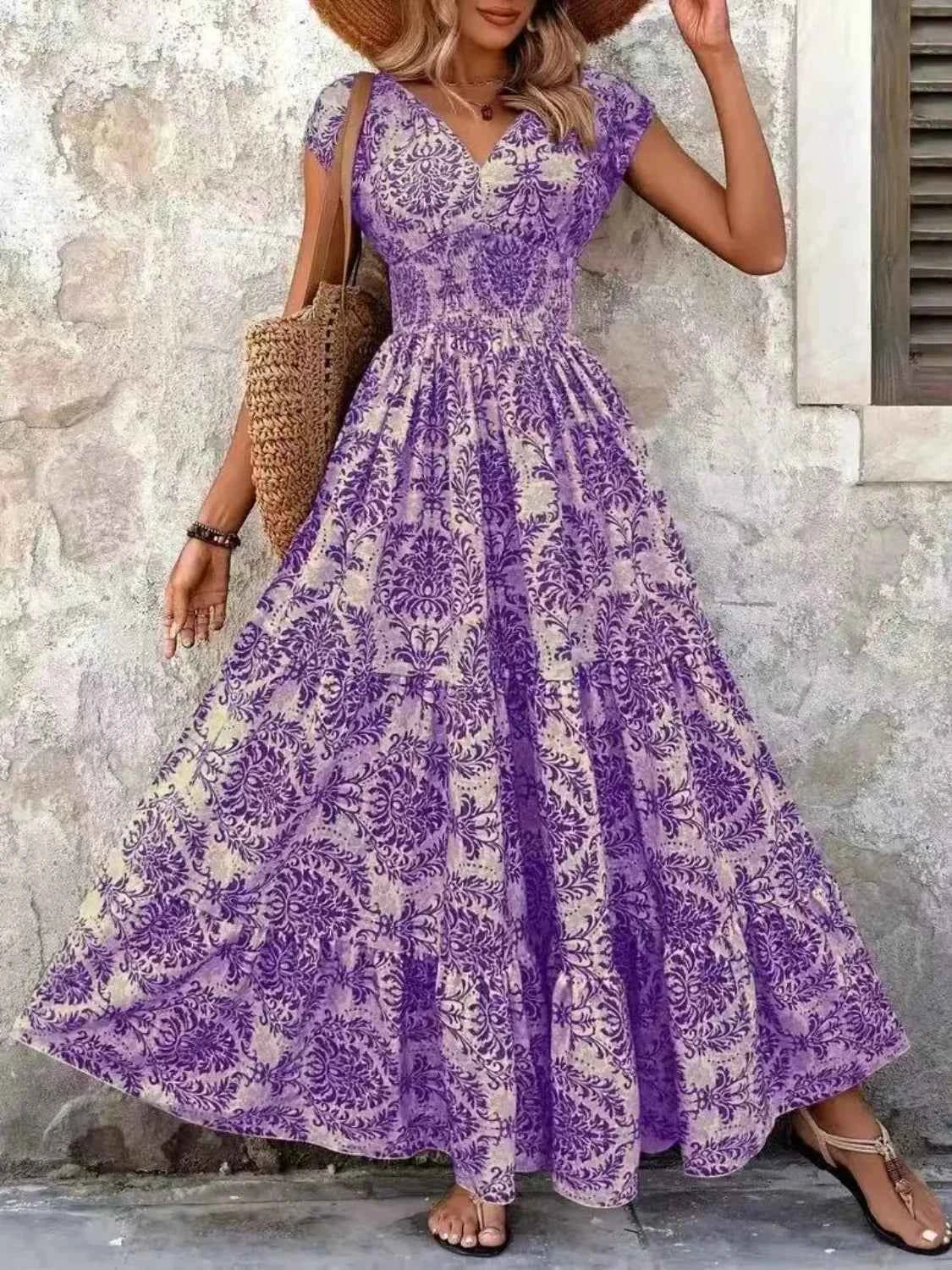Woman wearing a purple floral dress standing against a stone wall.